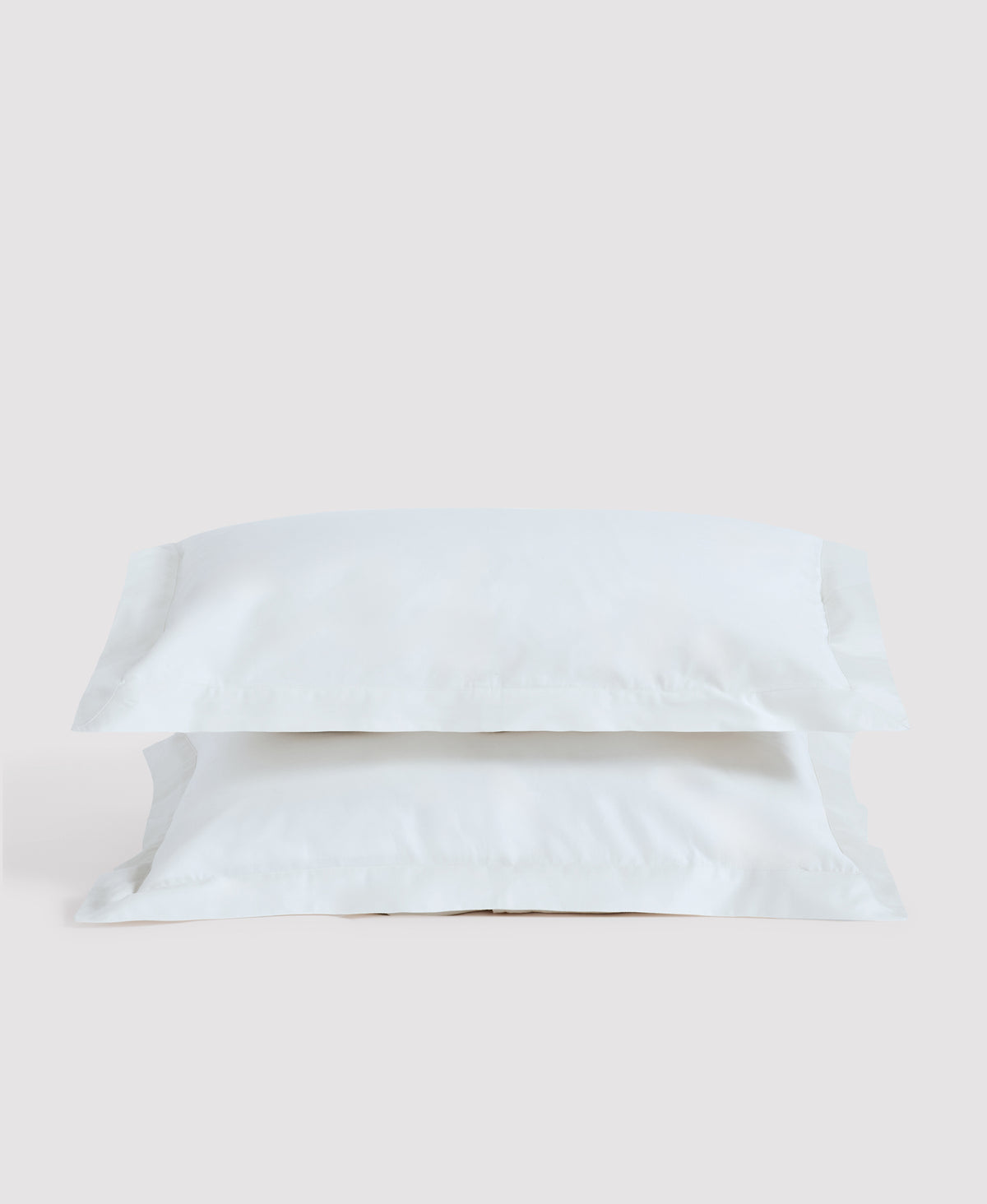 Two white linen pillows stacked against a light gray background in minimalist bedroom setting