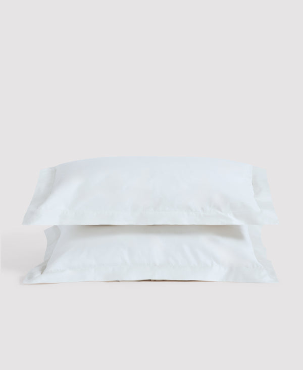 Two white linen pillows stacked against a light gray background in minimalist bedroom setting