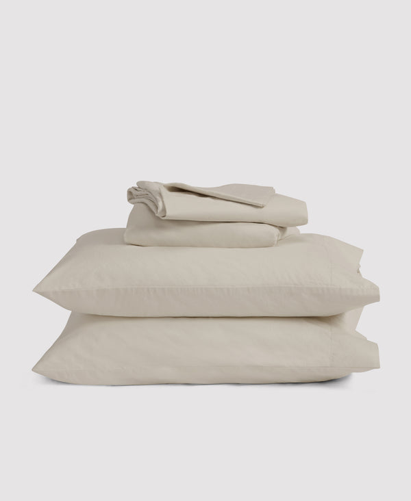 Stack of neatly folded beige linen bedding including pillowcases and sheets against white background