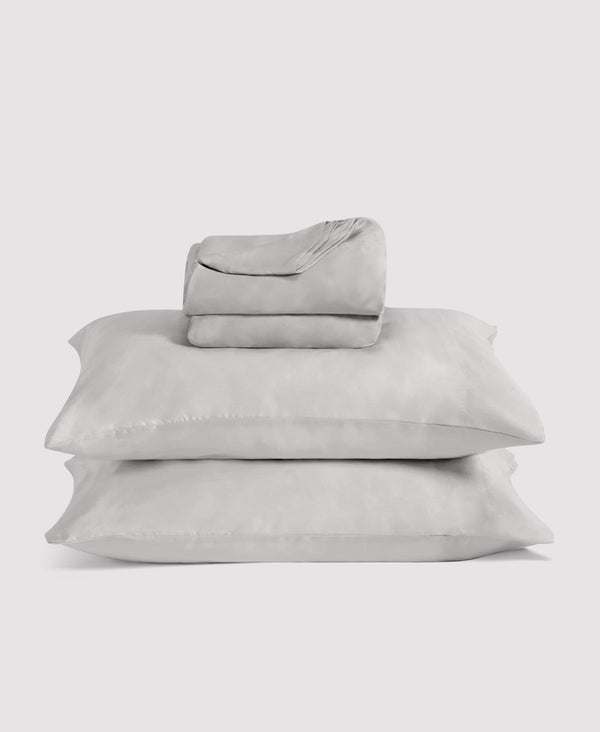 Stack of folded light gray bedding and pillowcases arranged on white background