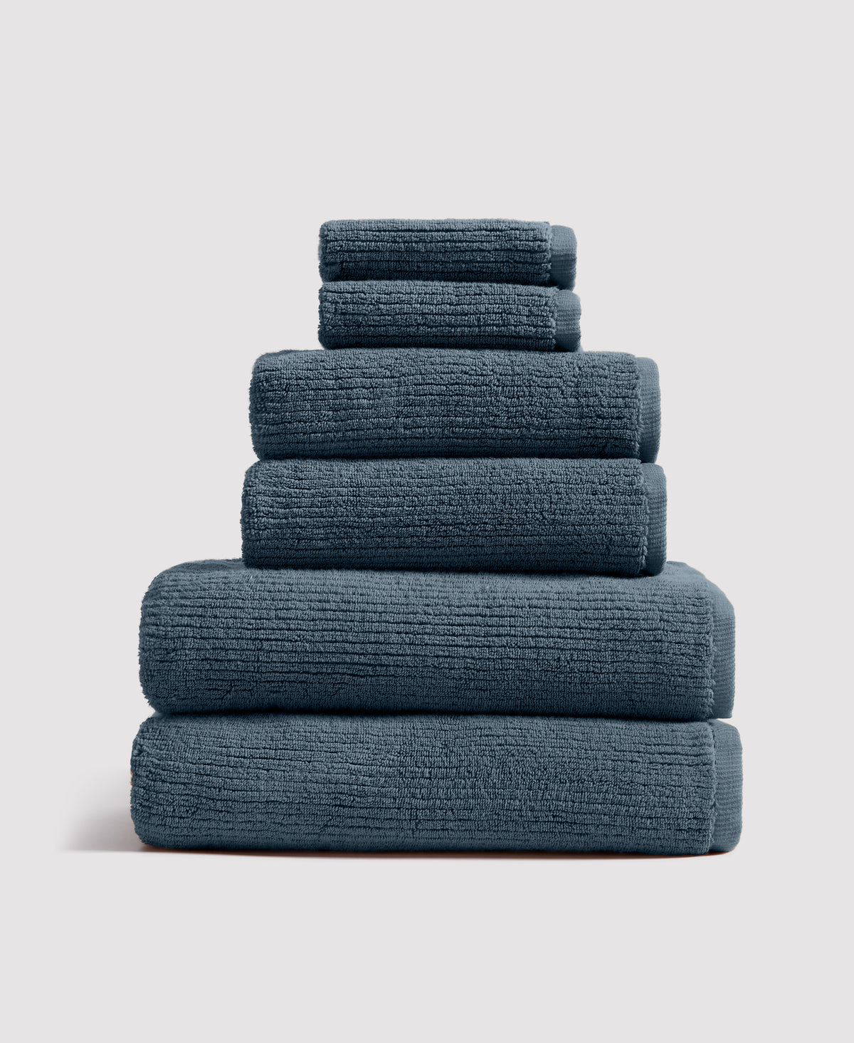 Stack of six neatly folded teal-gray towels arranged by size from largest at bottom to smallest at top