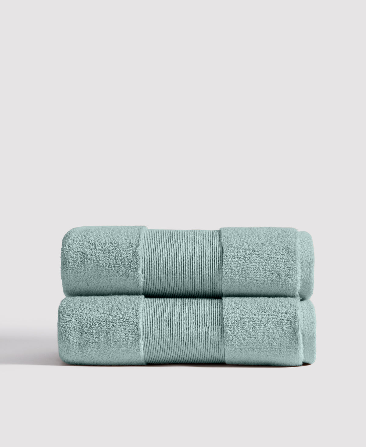 Two neatly folded sage green bath towels with ribbed borders stacked on white surface against light gray background.