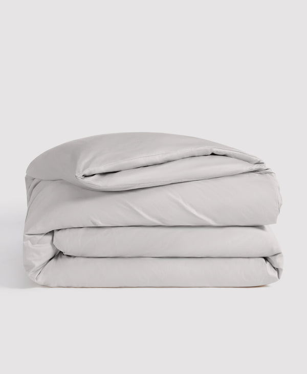 Light gray folded duvet cover and pillowcase bedding set stacked against white background