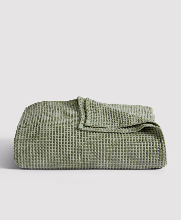 Sage green waffle-textured cotton blanket folded neatly against white background