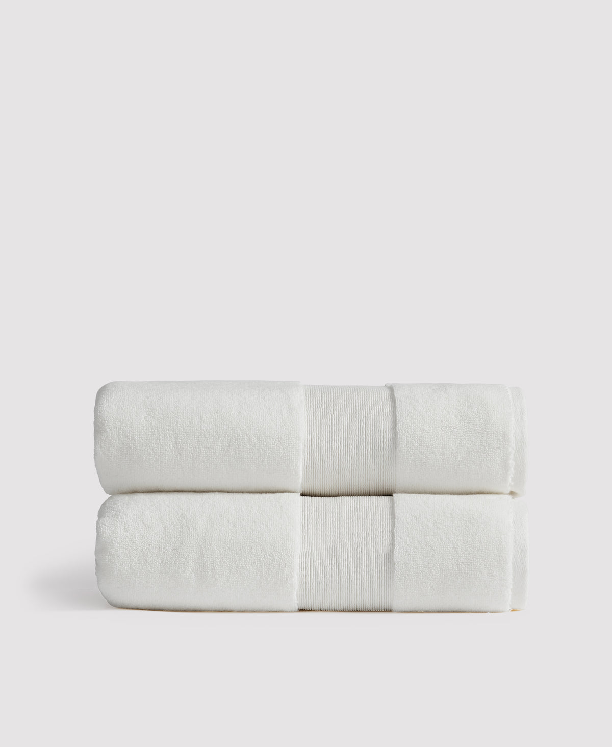 Two neatly folded white bath towels with gray decorative bands stacked on a white surface against a light gray background.