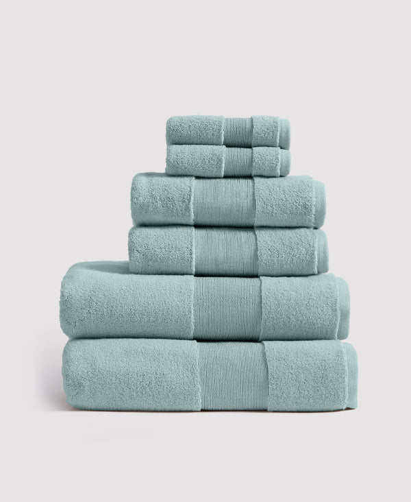 Stack of six sage green cotton towels with ribbed borders arranged in pyramid formation on white background