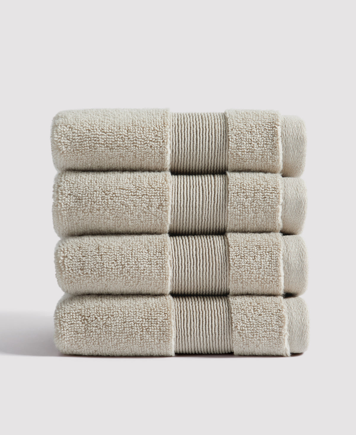 Stack of four beige towels with ribbed center stripe and terry cloth texture, neatly folded against white background