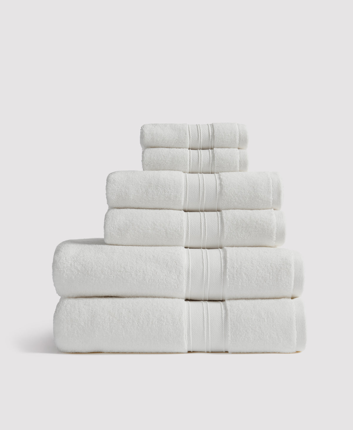 Stack of six neatly folded white towels with decorative striped borders arranged in pyramid formation against white background