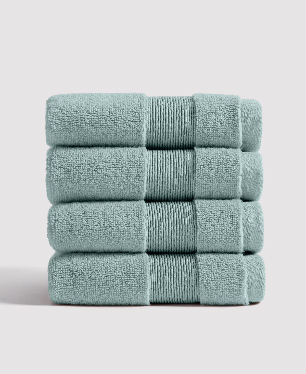 Stack of four sage green bath towels with ribbed decorative bands folded neatly on white surface