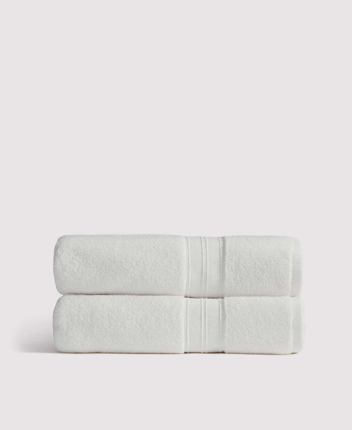Two neatly stacked white bath towels with decorative border stripes against a light gray background
