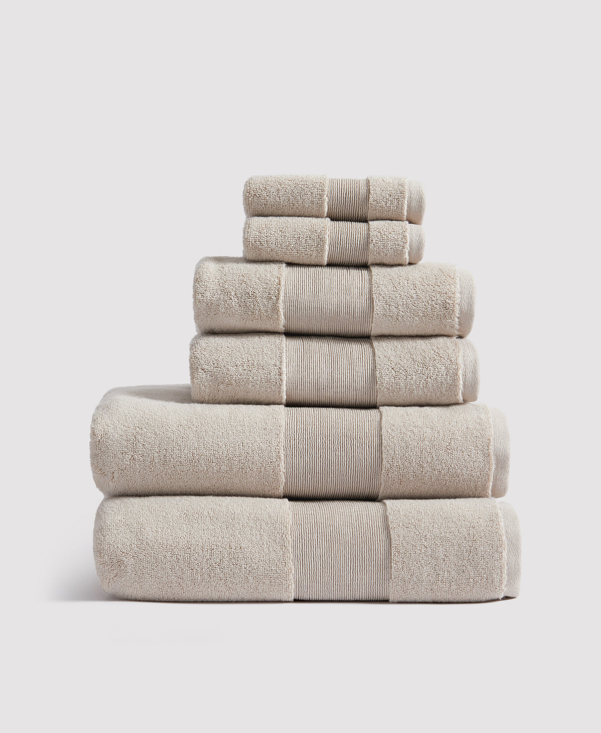 Stack of six beige terry cloth towels with ribbed borders arranged in pyramid formation against white background