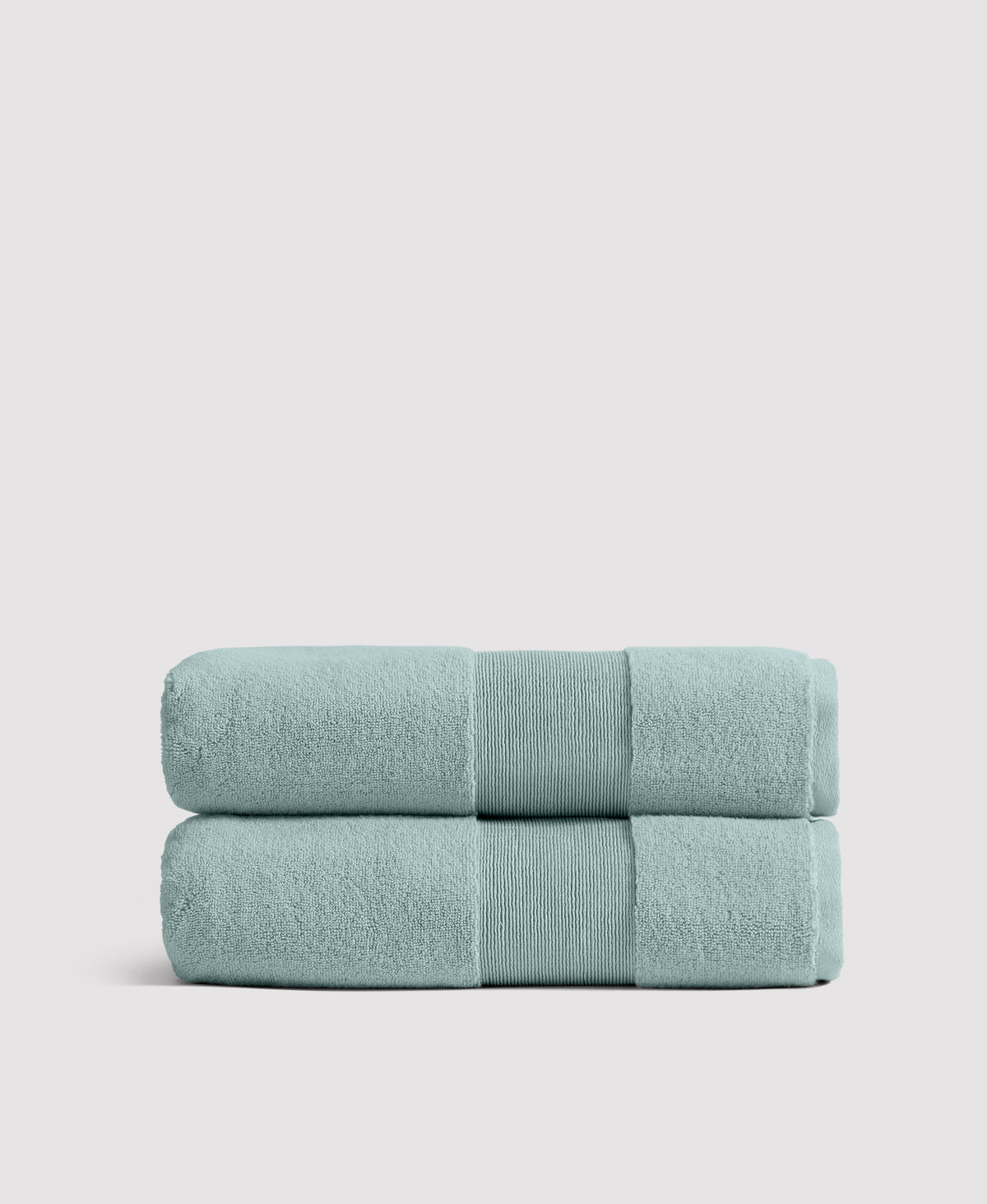 Two neatly stacked sage green bath towels with ribbed borders against a light gray background