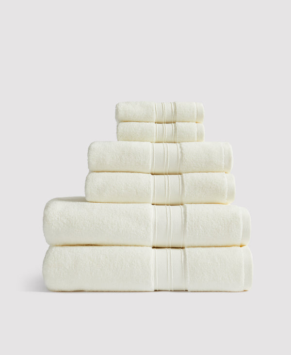 Stack of six cream-colored towels neatly folded and arranged by size against a light gray background