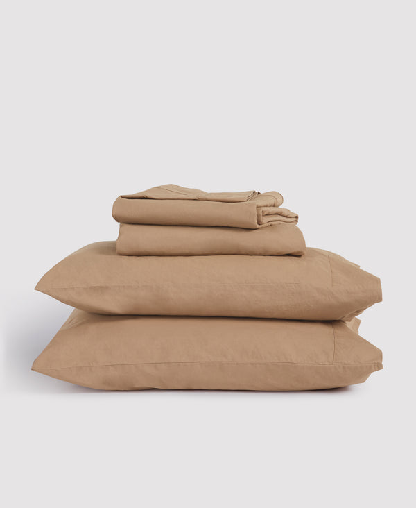 Stack of folded beige bedding set including pillowcases and sheets against white background