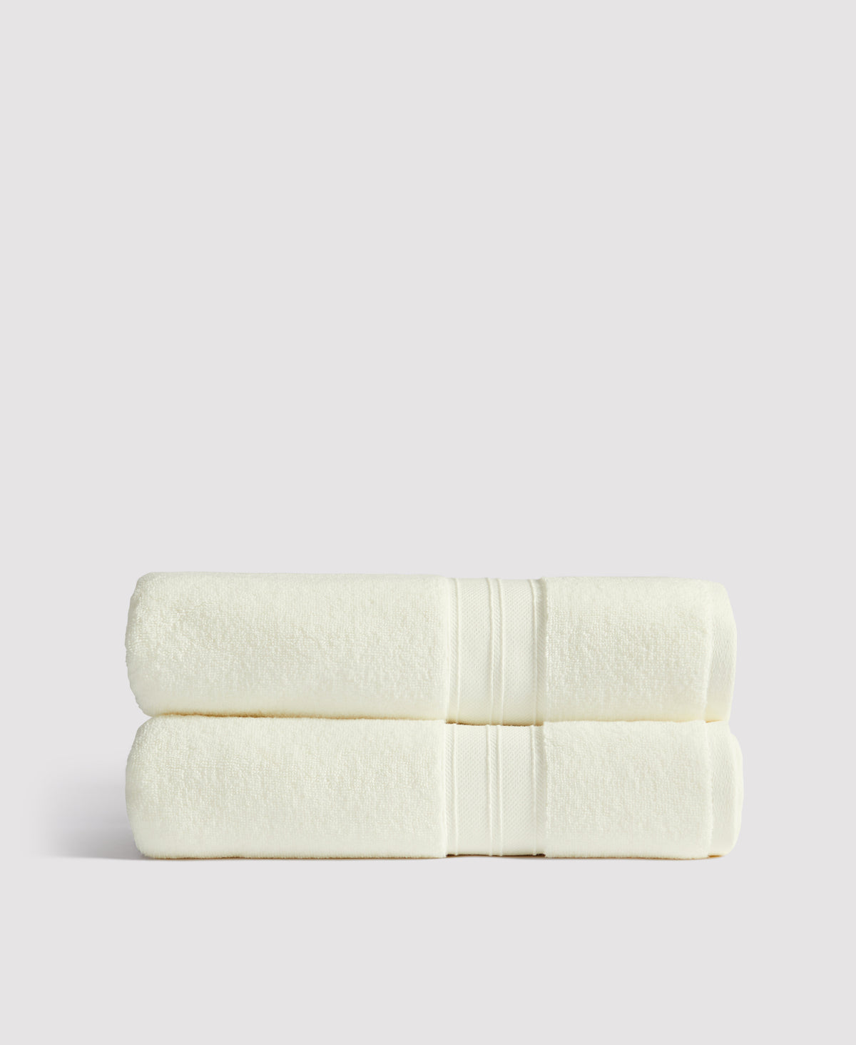 Two neatly folded cream-colored towels with white stripe detail stacked on white surface against gray background