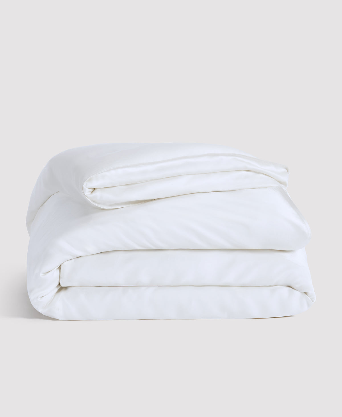 White folded comforter or duvet neatly stacked against a light gray background