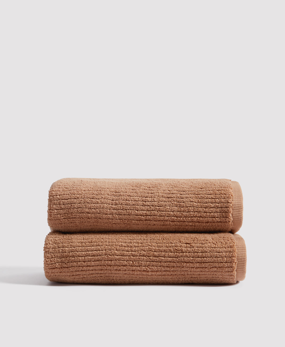 Two neatly folded brown textured towels stacked on white surface against light gray background