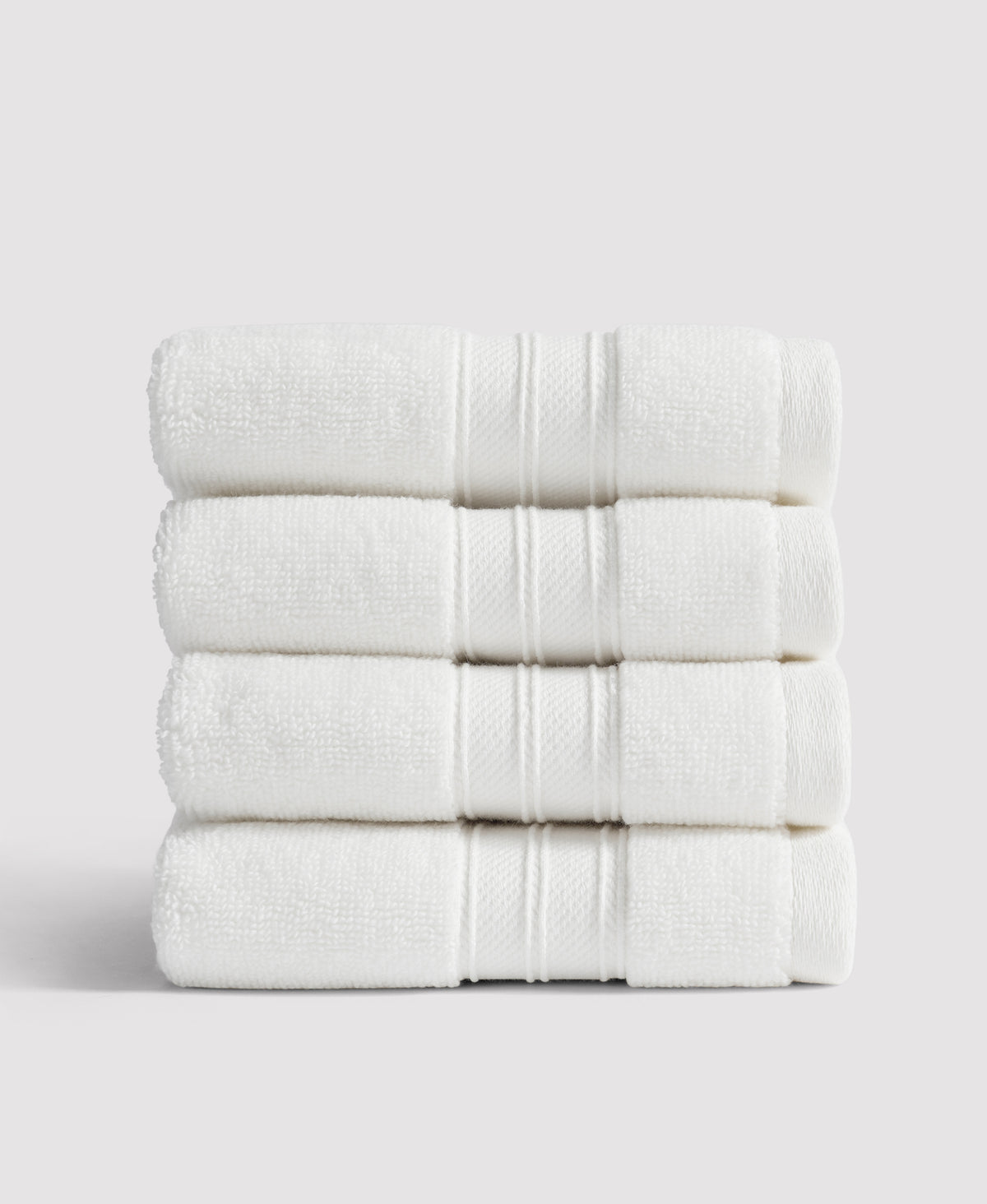 Stack of four neatly folded white towels with decorative border stripes against white background