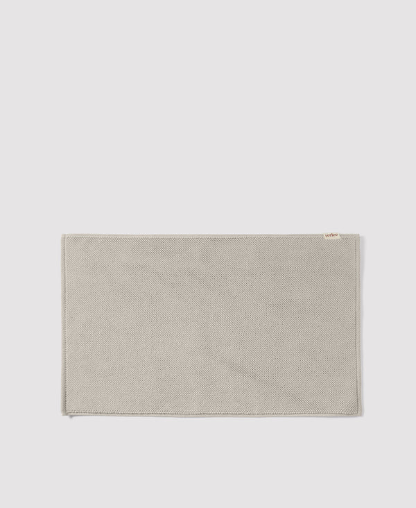 Olive green woven textile placemat with herringbone pattern and small white label on light gray background