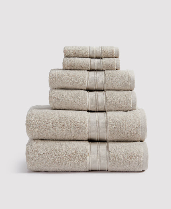 Stack of six beige cotton towels with decorative border stripes, arranged by size from largest to smallest
