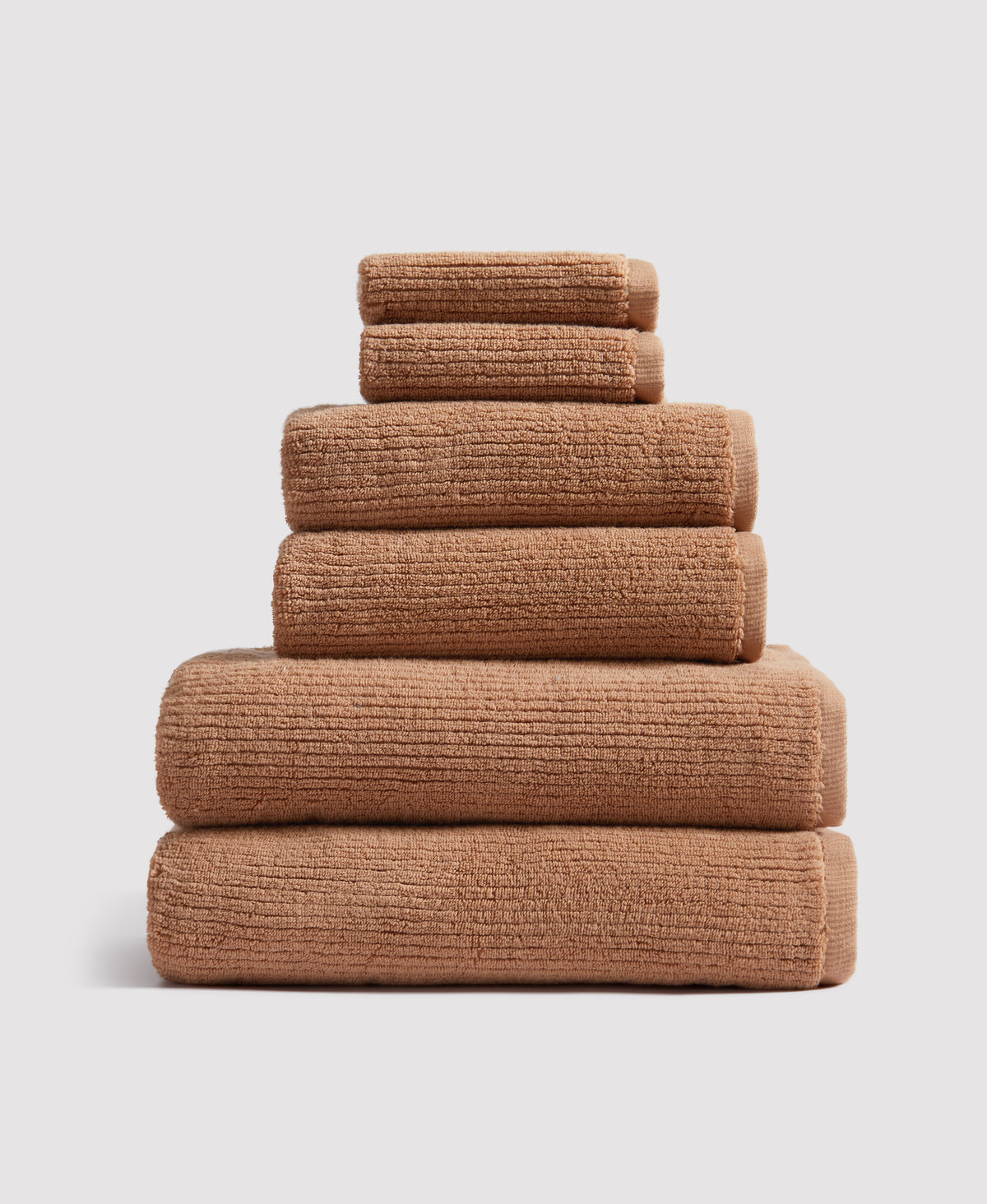 Stack of six neatly folded brown textured towels arranged in pyramid formation against white background