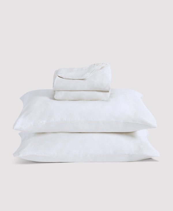 Stack of white linen bedding including pillowcases and sheets neatly folded against a light gray background