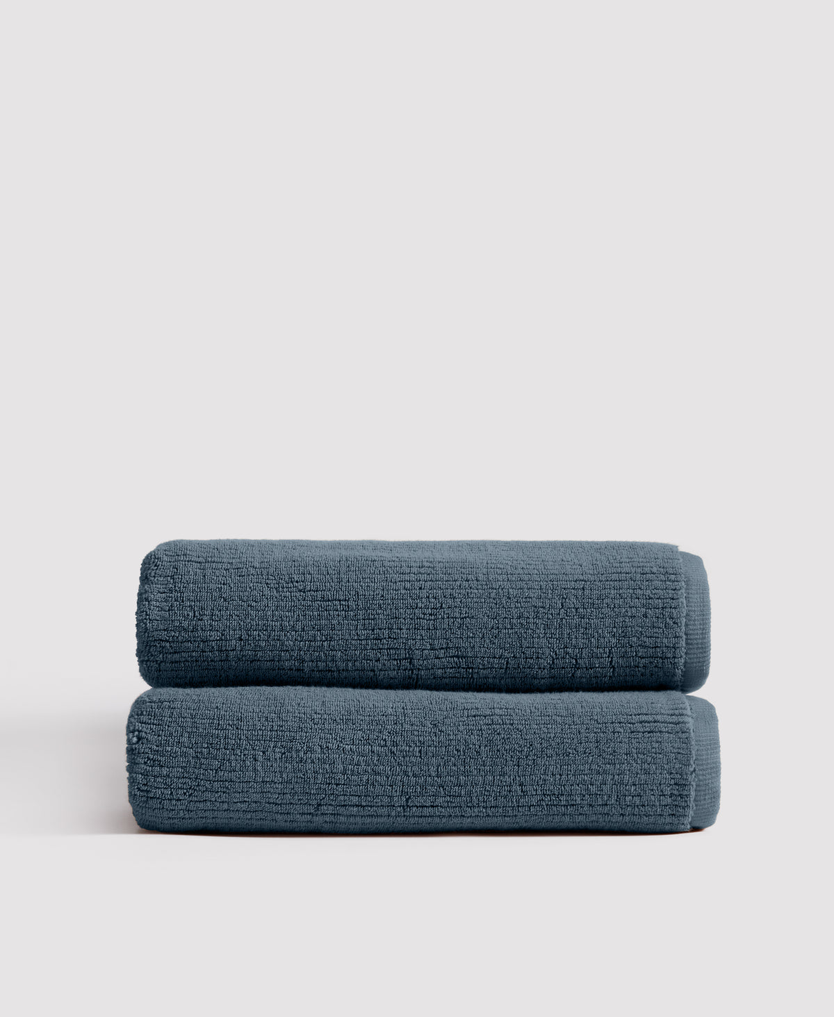 Two neatly stacked teal blue textured towels against a white background