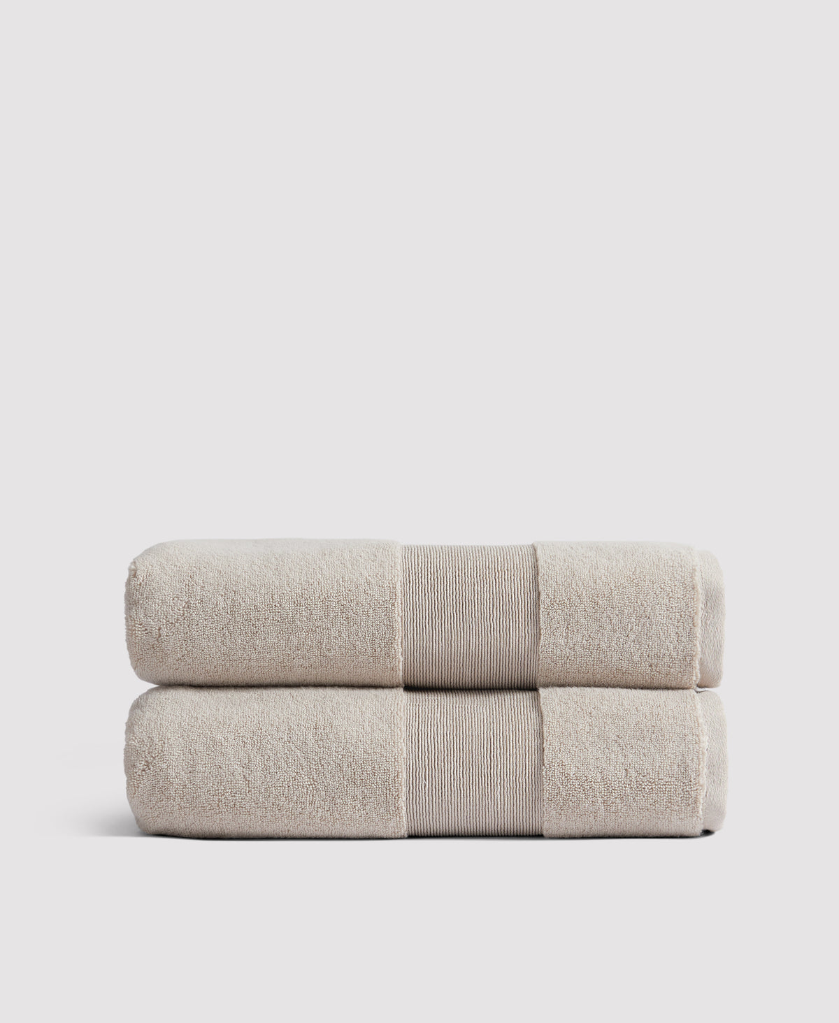 Two neatly folded beige towels with ribbed borders stacked on a white surface against a light gray background.