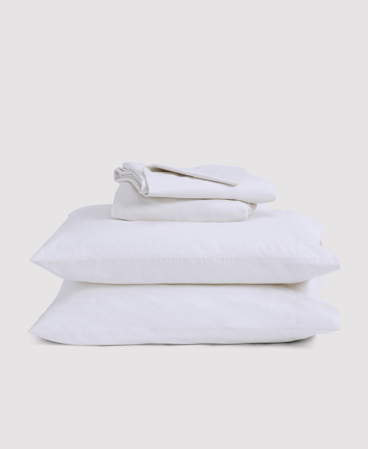 Stack of neatly folded white bed linens including fitted sheet, flat sheet and pillowcases against light gray background